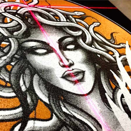 Digital print with black, white and orange gradient graphic of medusa on a black garment with printer lazer in foreground.