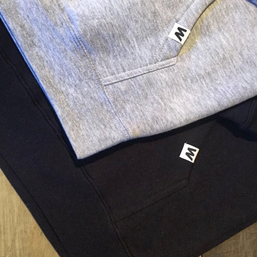 White W hem tags on grey and black hoodie on wood background.