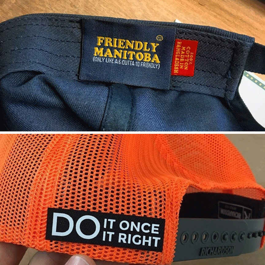 Navy cap with Friendly Manitoba (Only like as outta 10 friendly) and orange cap with Do it once do it right. Both on wood backgrounds.