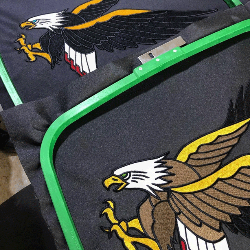 Two large eagle embroideries on black fabric with embroidery green frames still on.