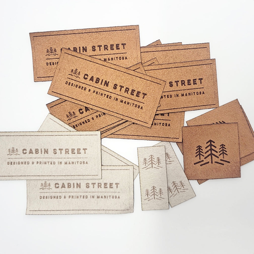 Pile of beige and tan Microsuede Cabin Street Designed and printed in Manitoba tags on white background.